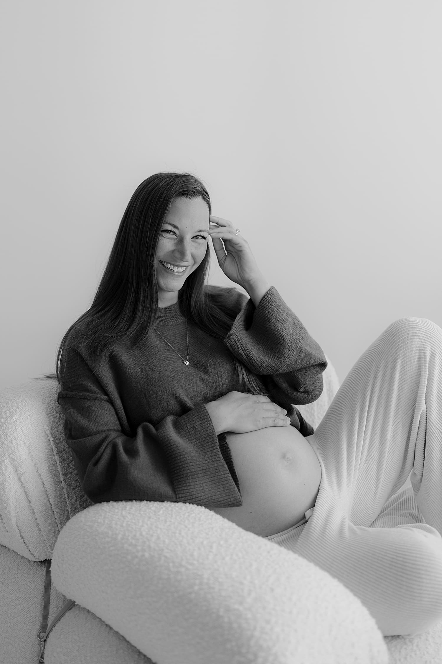 woman in sweats cradles her belly for studio maternity shoot