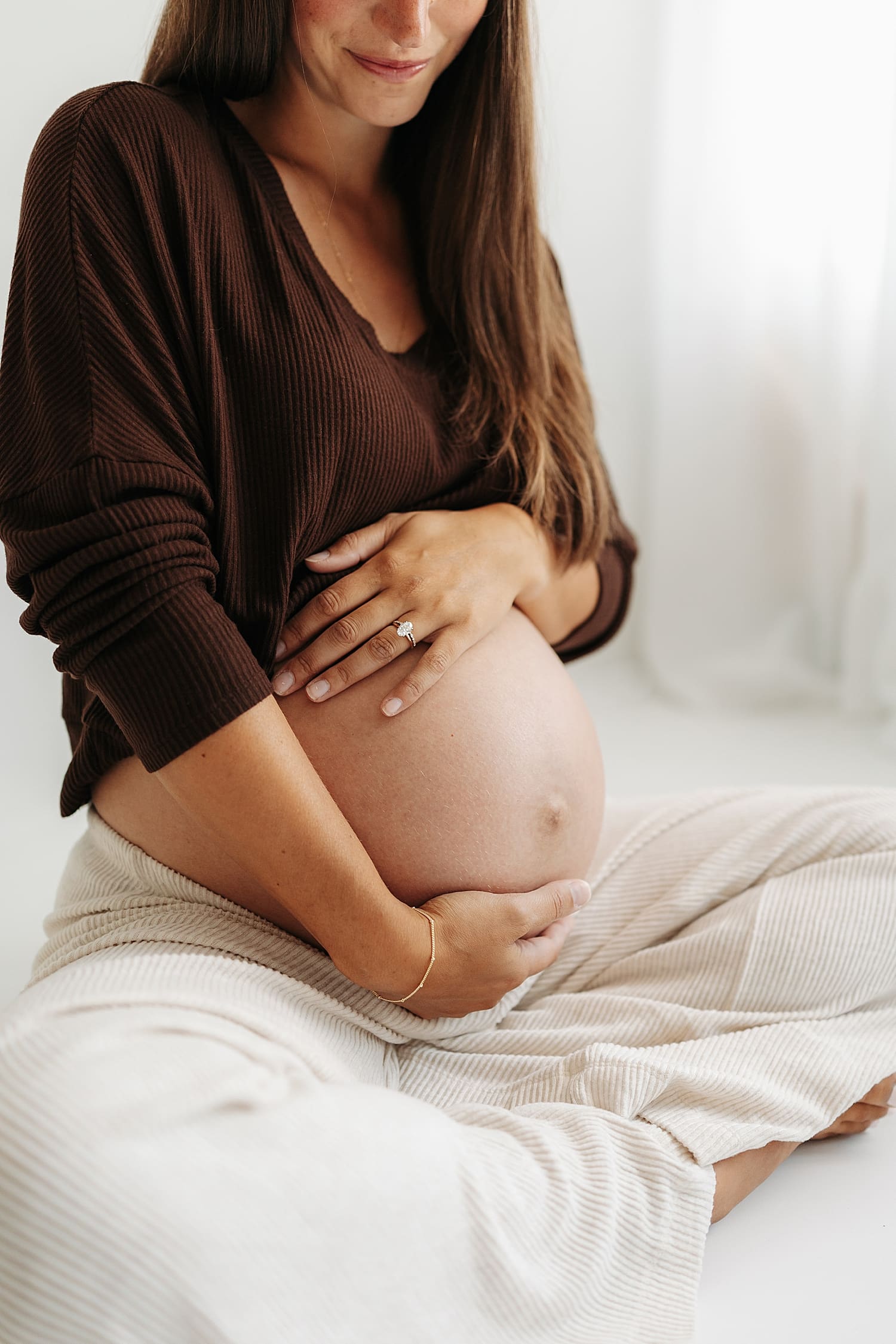 brunette cradles her bump while sitting on floor by Wisconsin family photographer