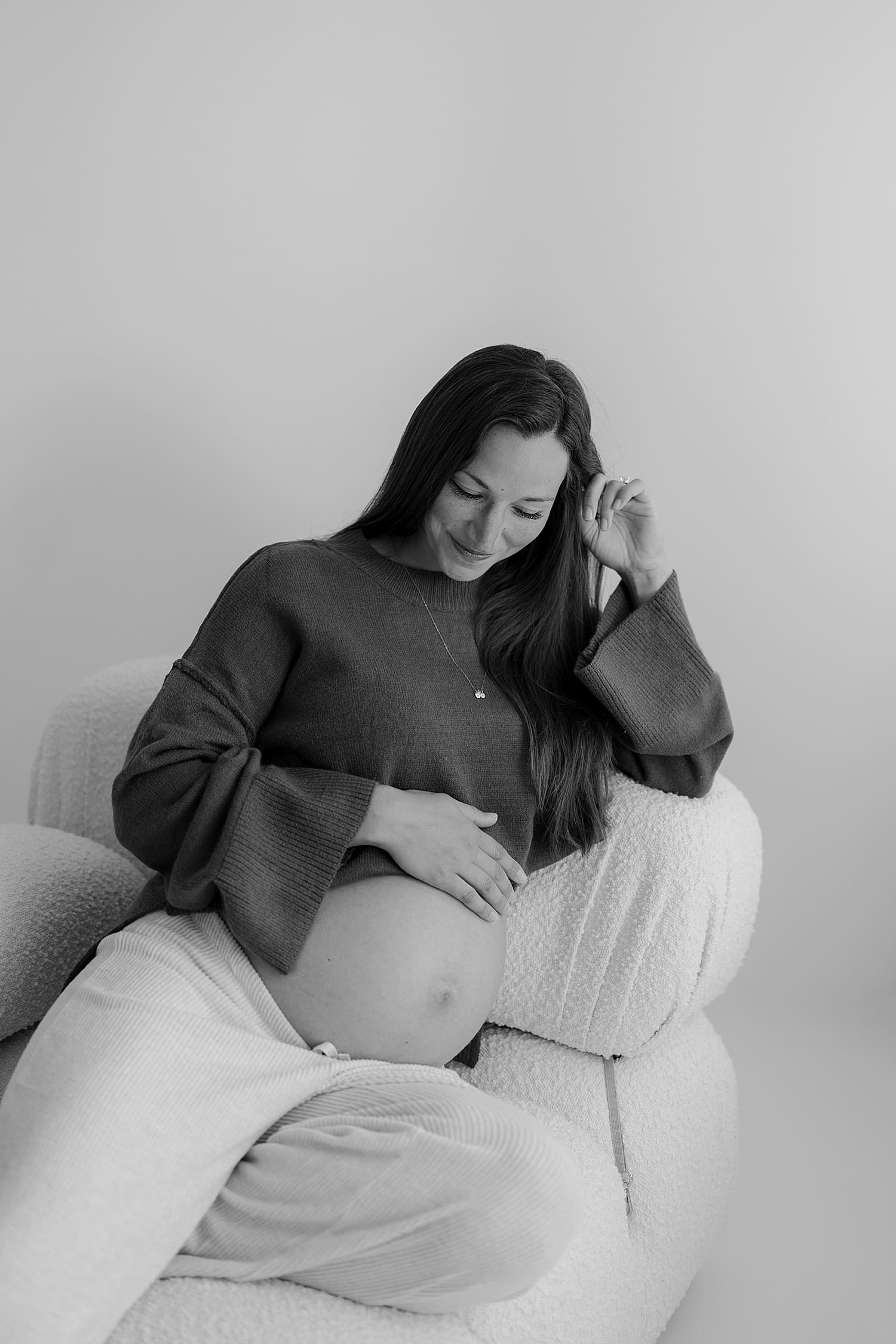 pregnant mama gazes down at bump on couch by Rose and Oak Photography 