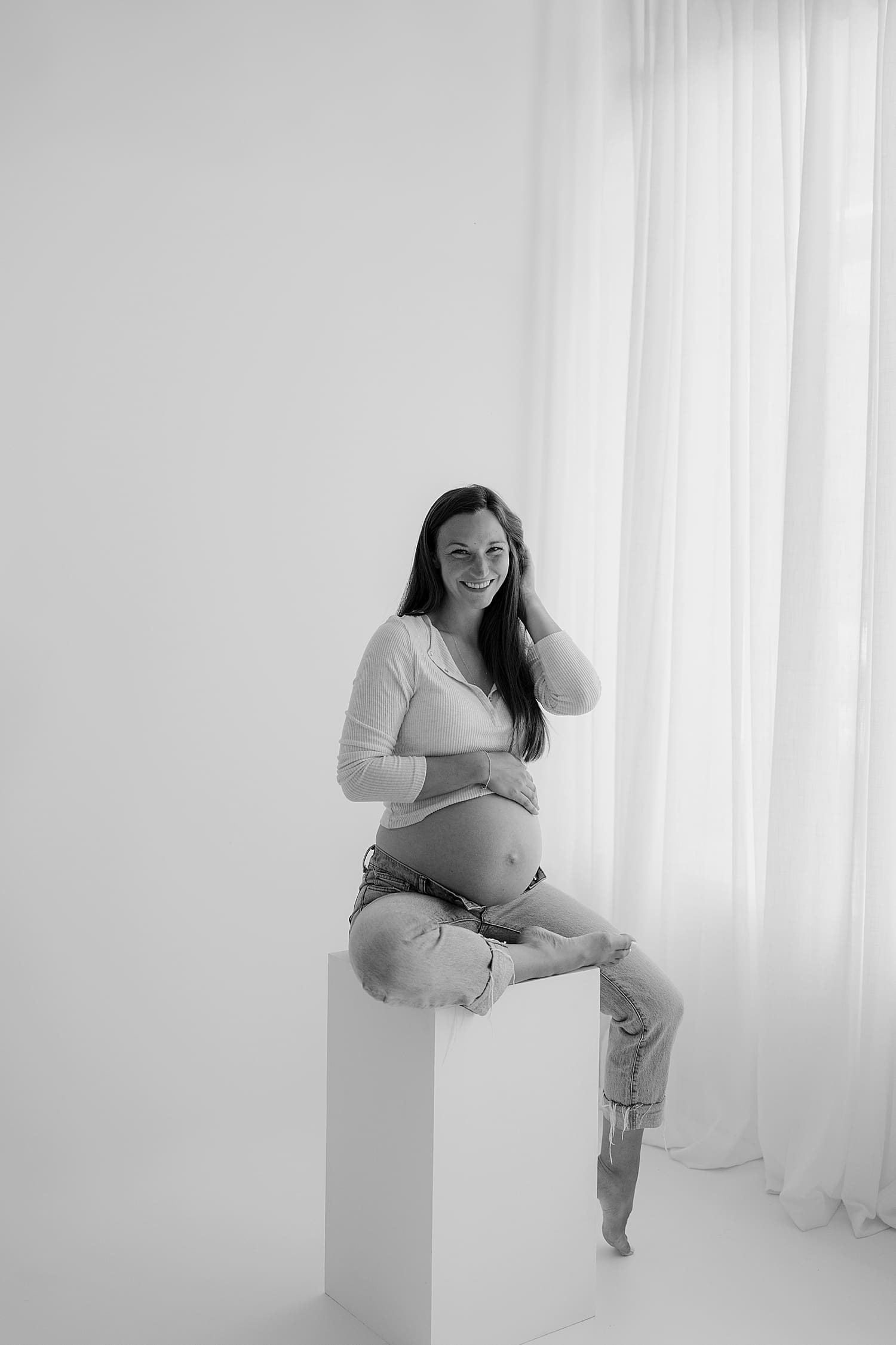 mother sits on stool in front of big windows by Rose and Oak Photography 