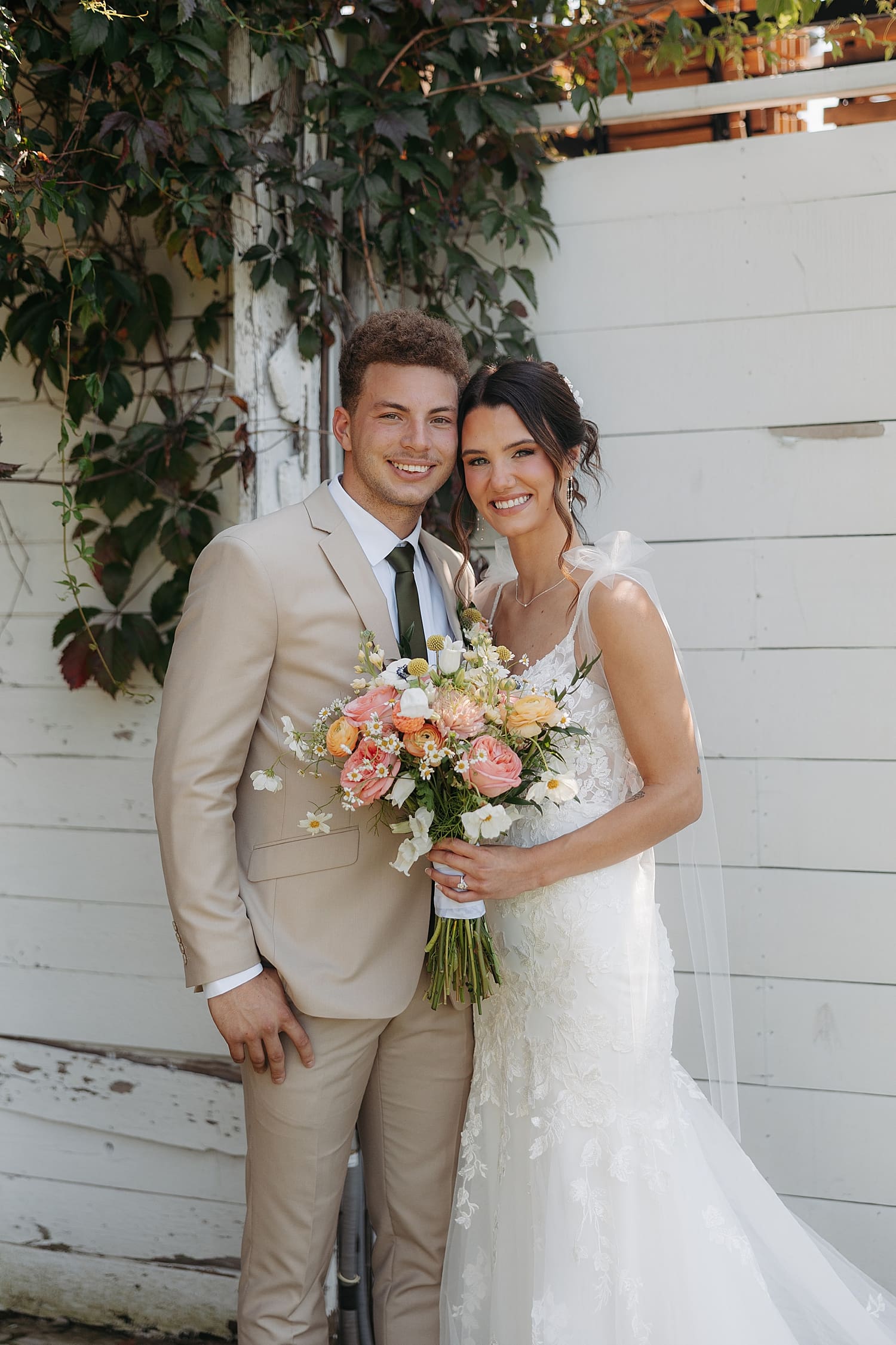 brunette bride stands in front of white wall with groom by Wisconsin wedding photographer