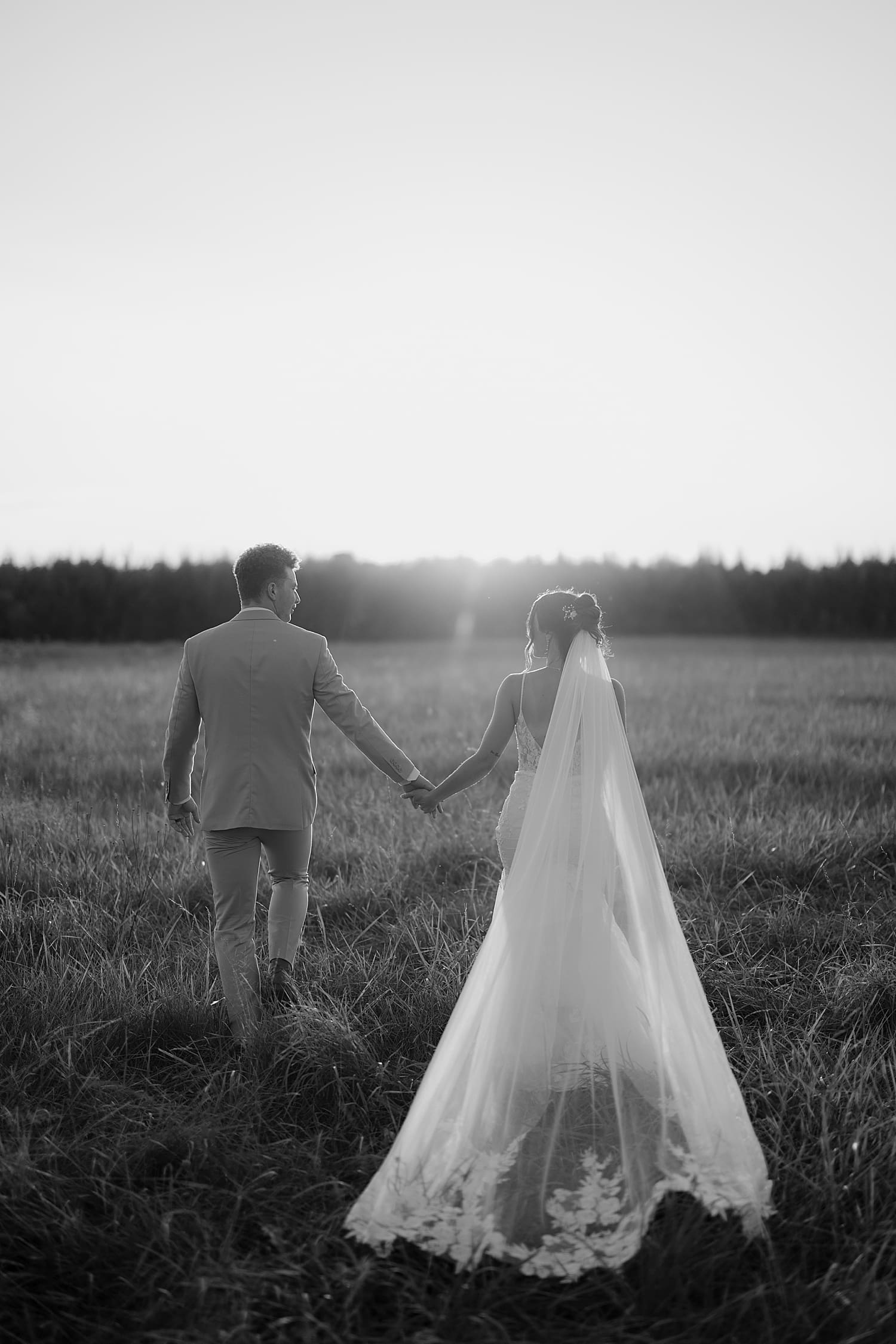 newlyweds walk through a field during golden hour at Ivory North Co.