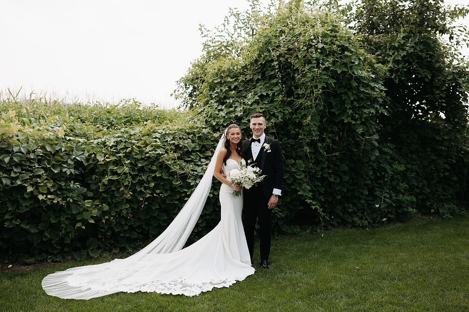 bride and groom stand together in front of ivy by Rose and Oak Photography