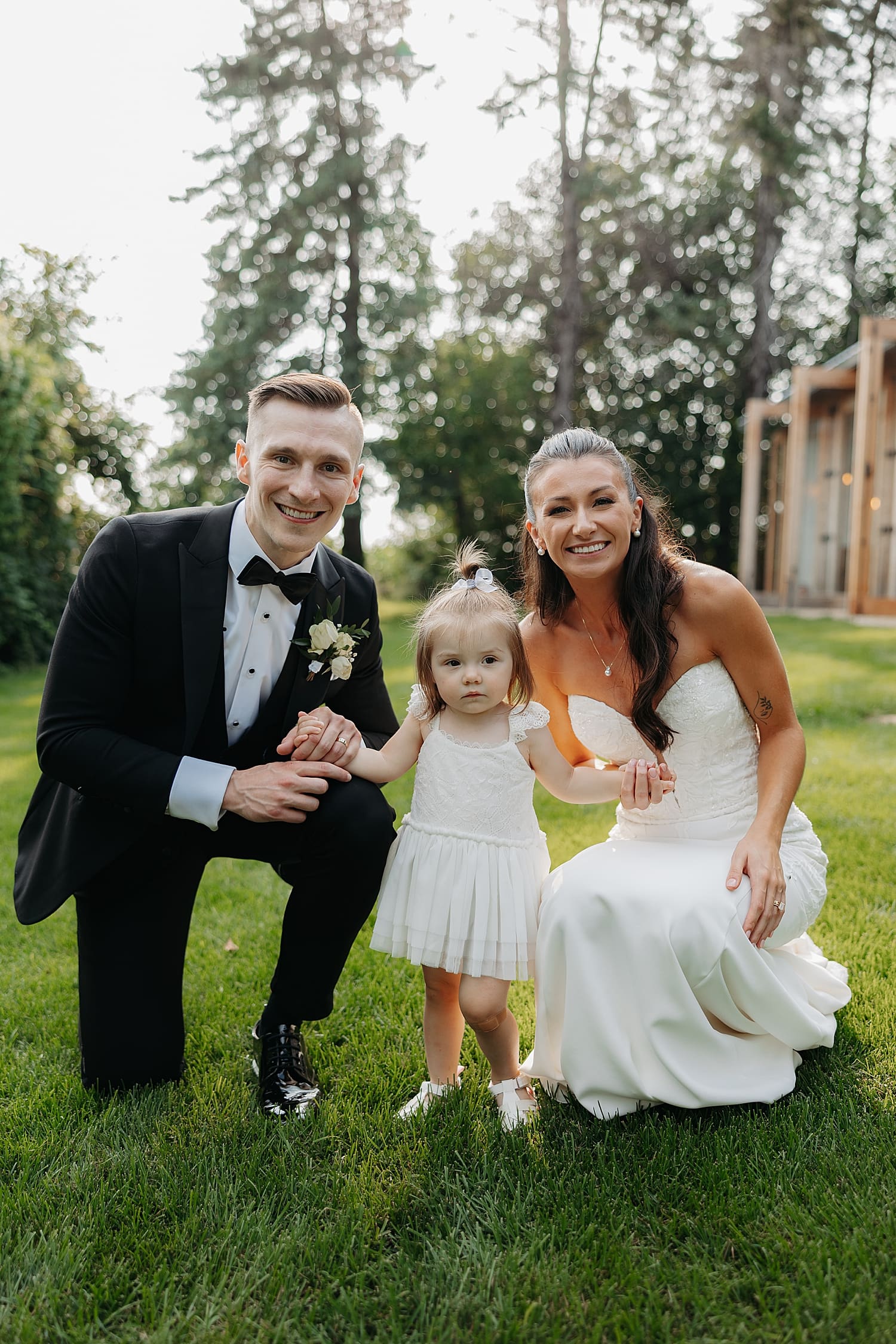 newlyweds kneel in grass with their toddler daughter by Wisconsin wedding photographer