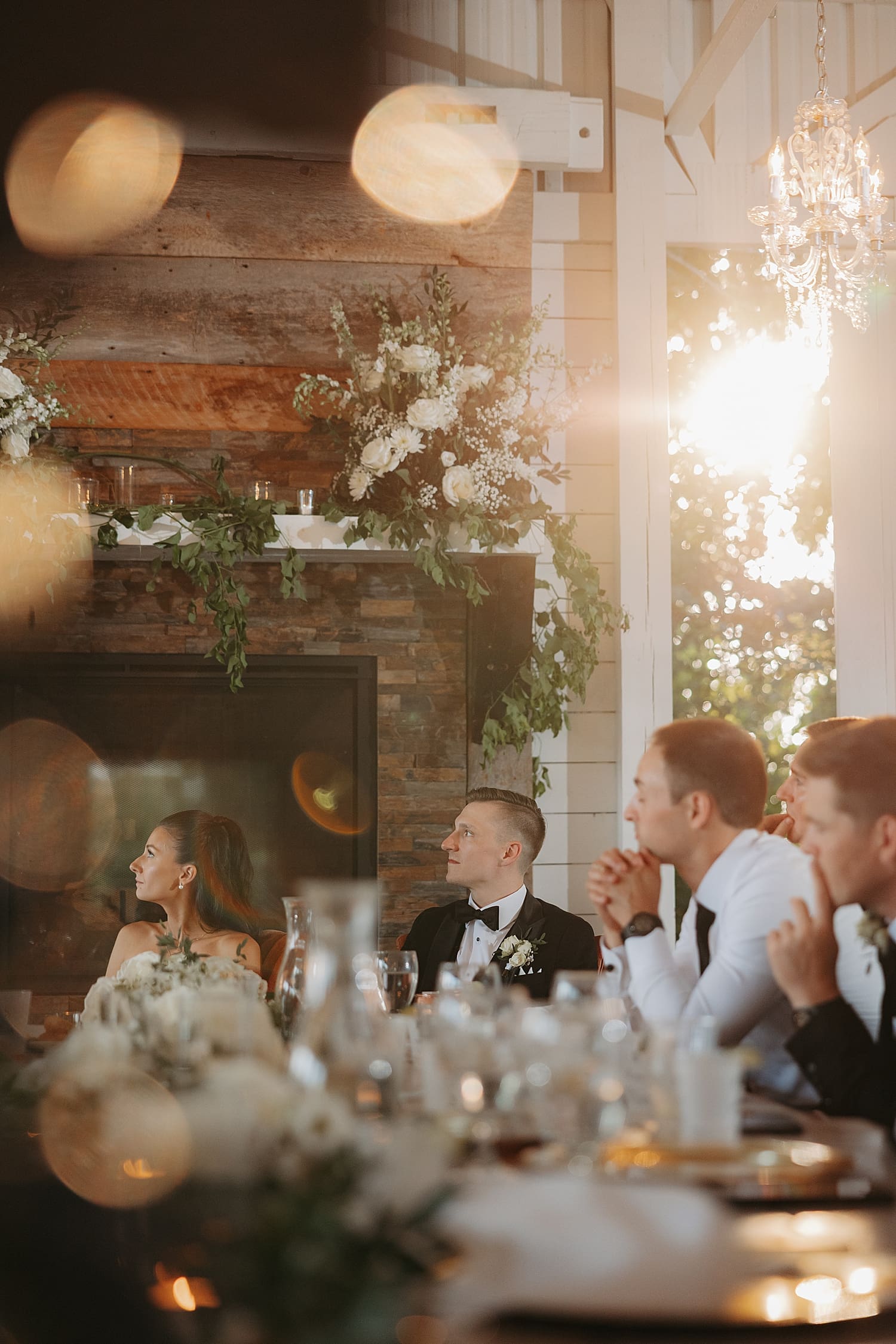 husband and wife listen to toasts at reception under twinkle lights by Wisconsin wedding photographer