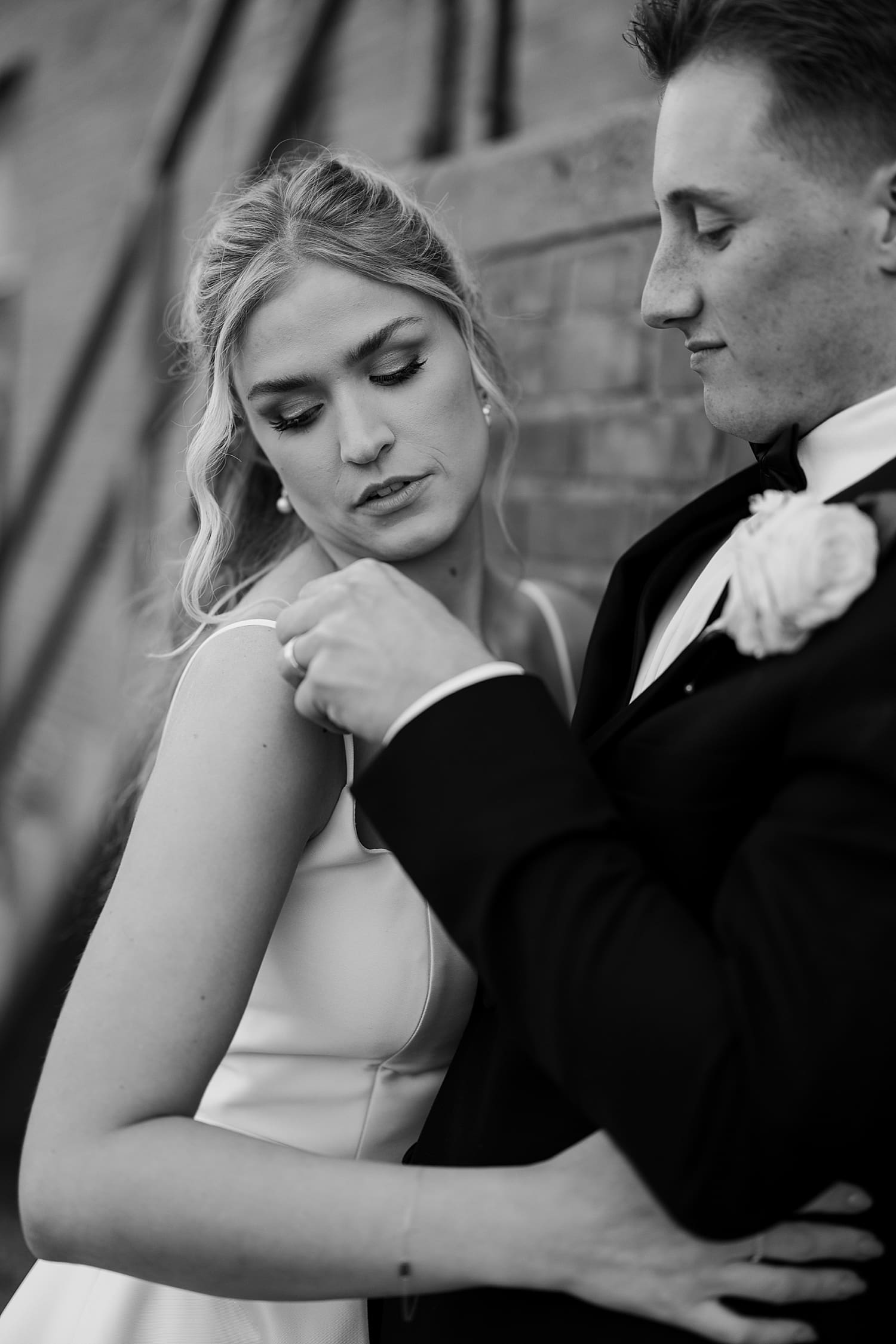 bride looks over her shoulder as groom adjusts her dress strap by wisconsin photographer