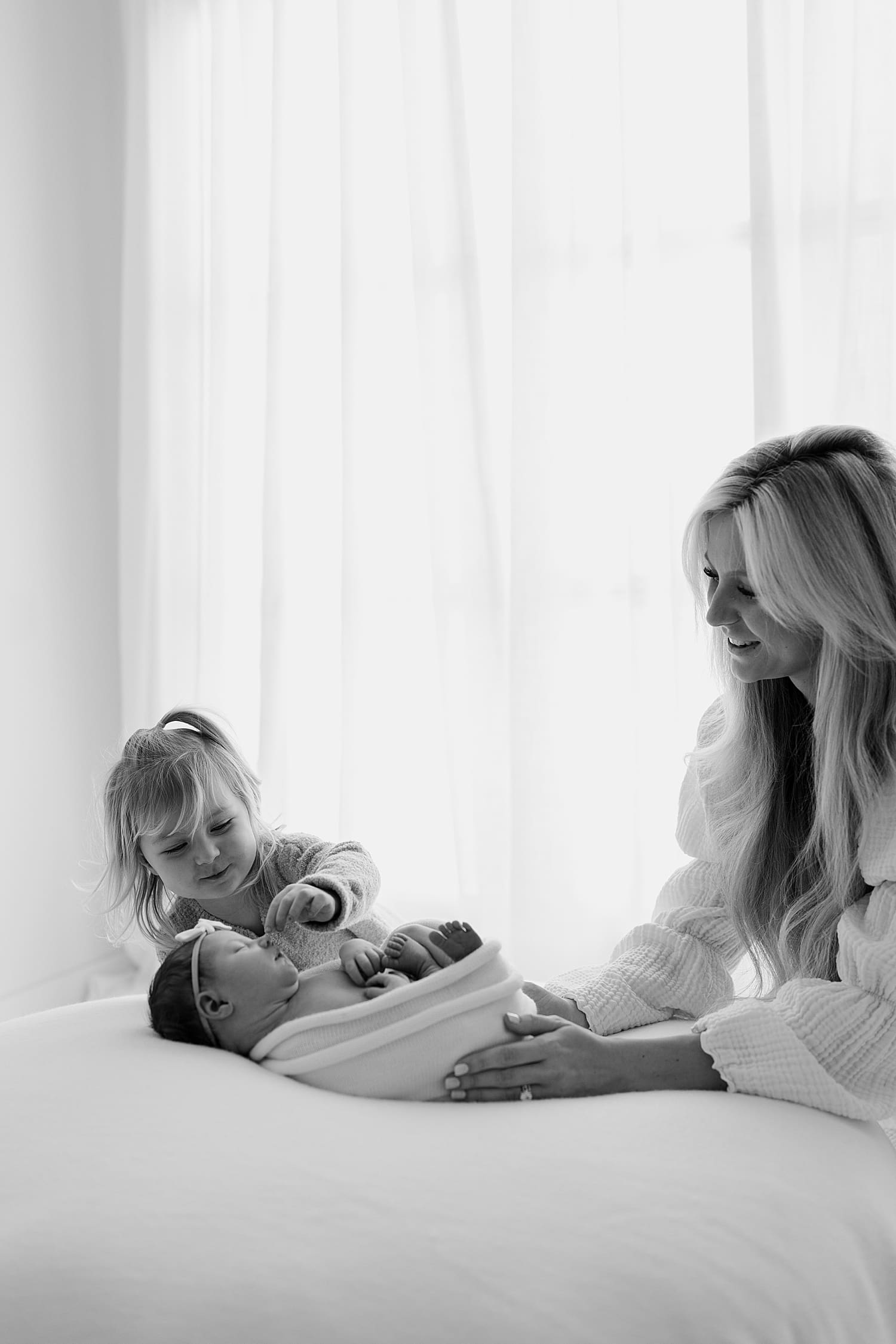 mother helps toddler touch new baby by Rose and Oak Photography