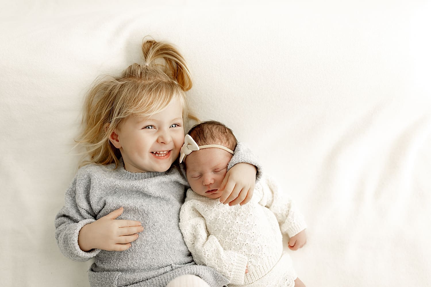 toddler hugs baby in white sweater by Rose and Oak Photography