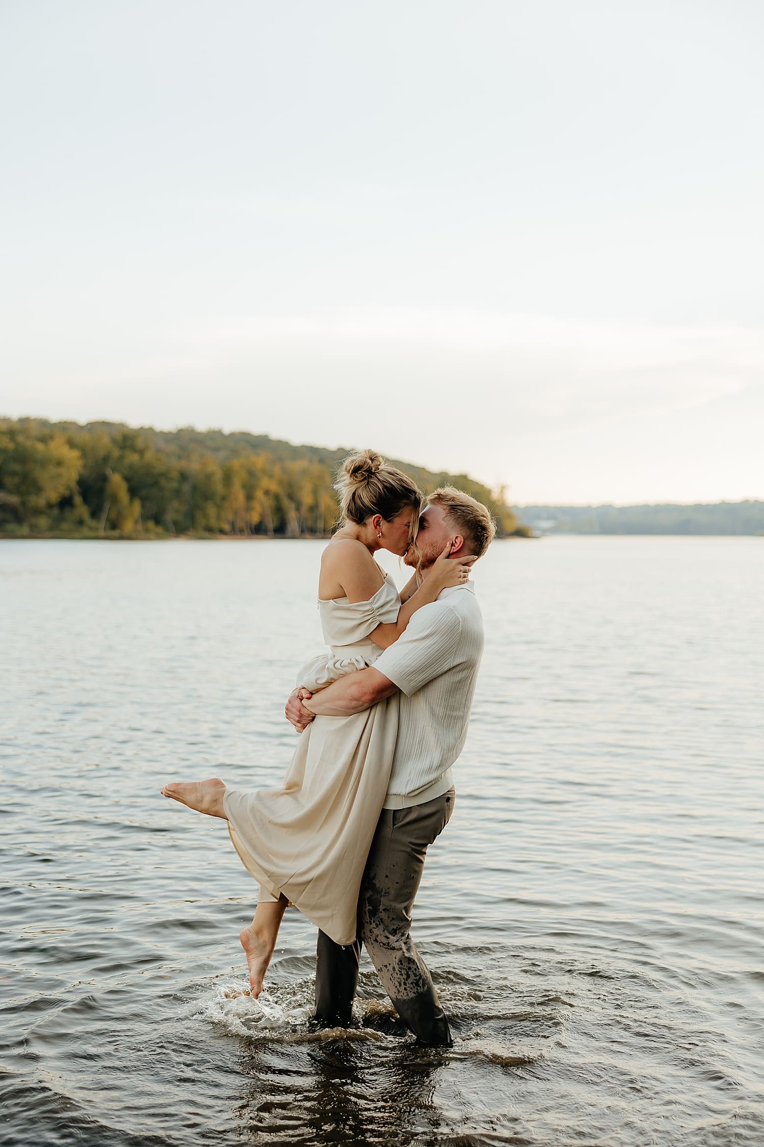 man lifts ups woman in water to kiss her by Rose and Oak Photography