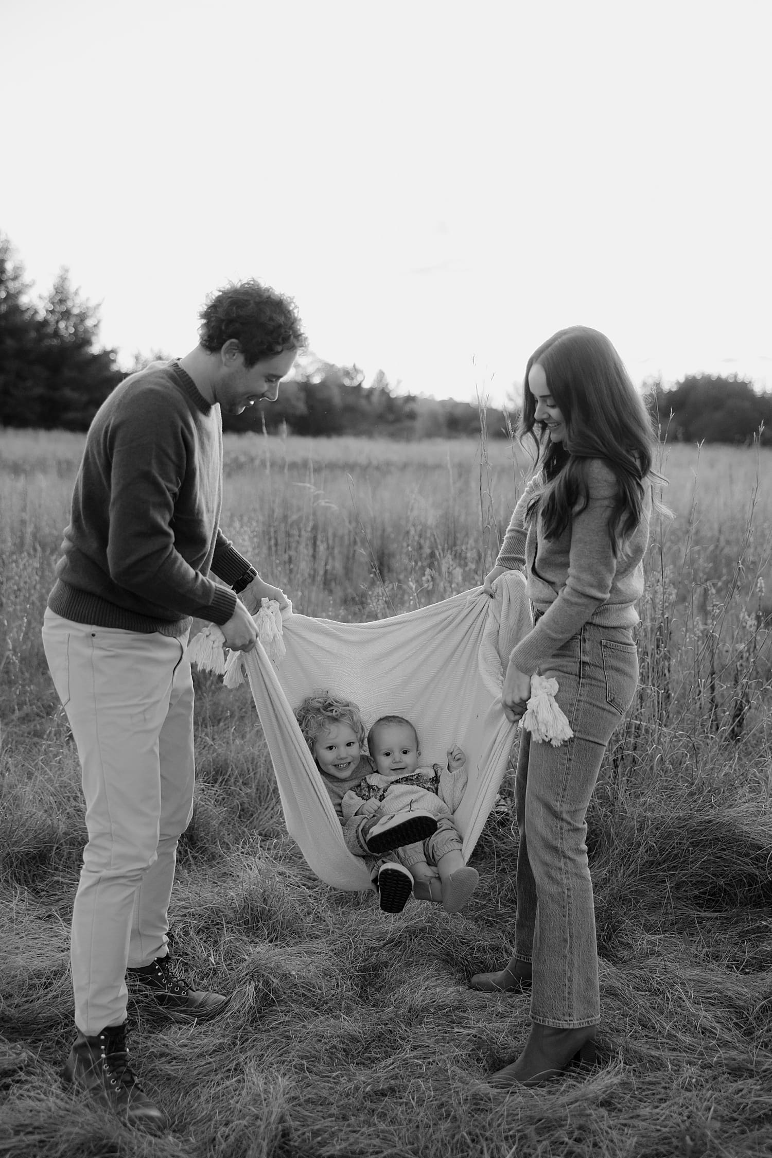 mother and father rock their kids in blanket outside by Rose and Oak Photography