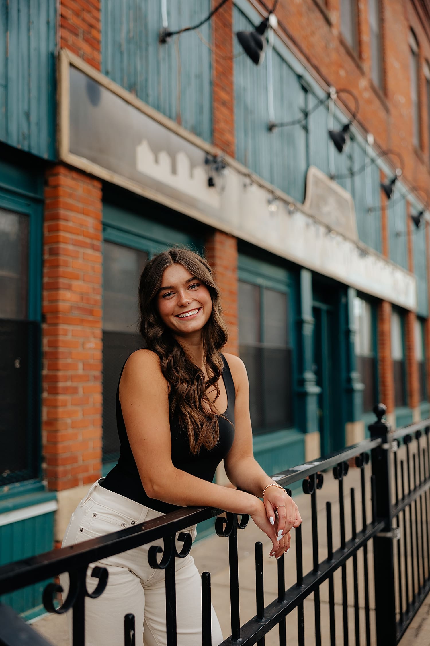 brunette leans against city railing downtown by Rose and Oak Photography