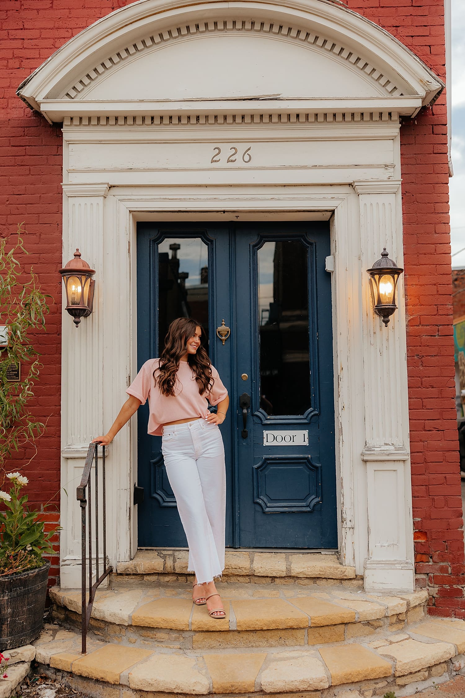 graduating person stands in front of blue door by Wisconsin photographer