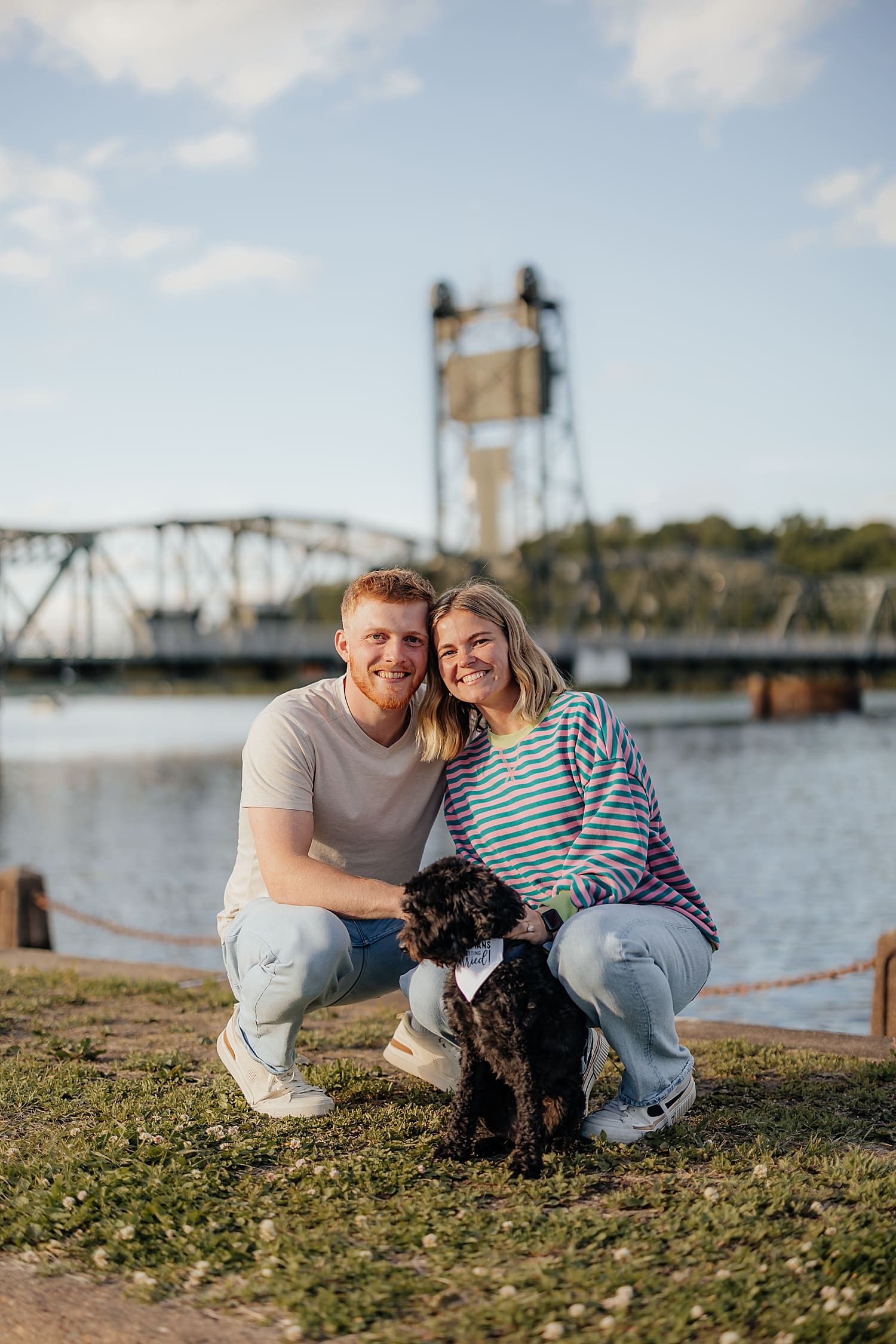 engaged couple kneels with their pup by Wisconsin wedding photographer