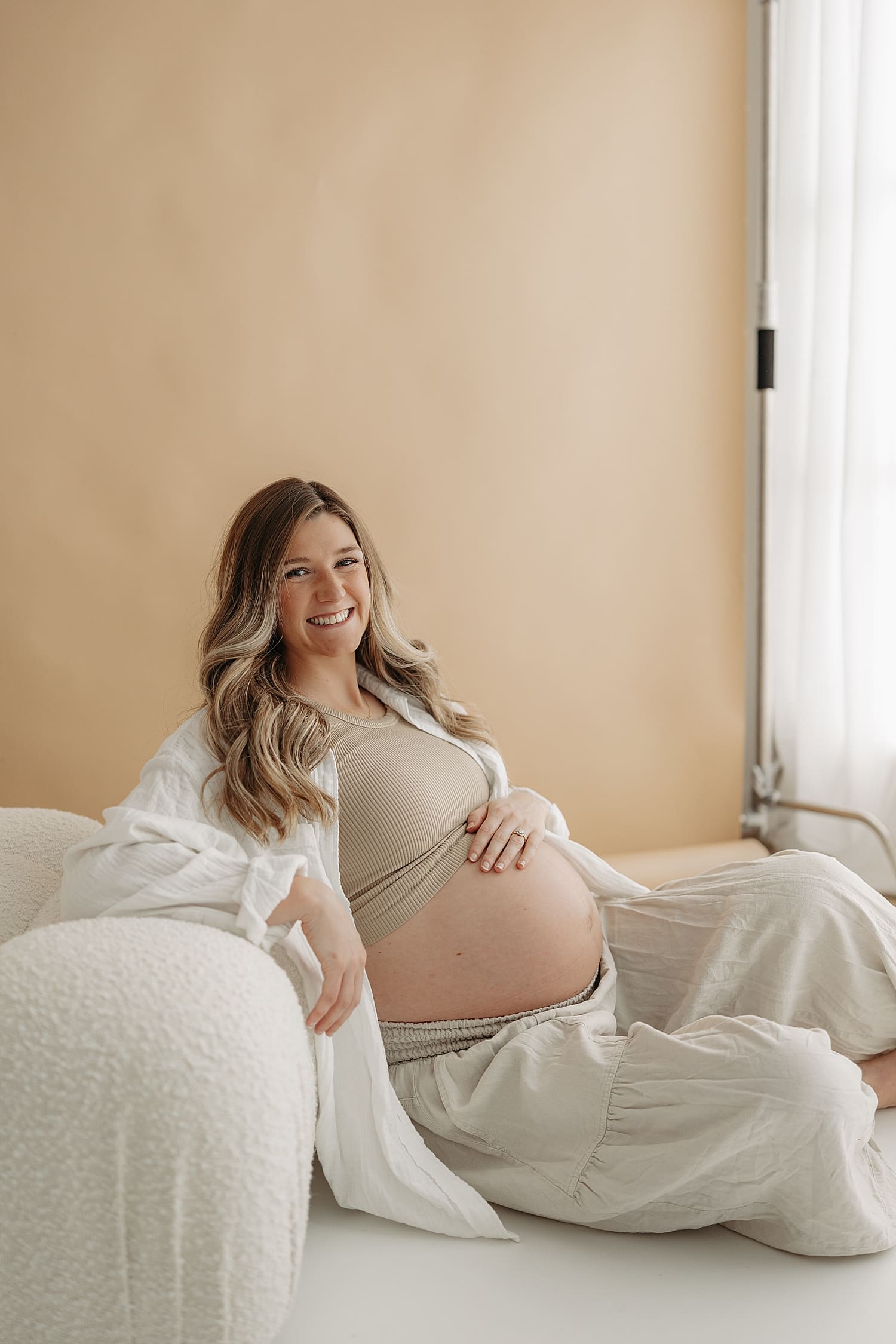 blonde woman sits on floor in neutral clothing for classic studio maternity session