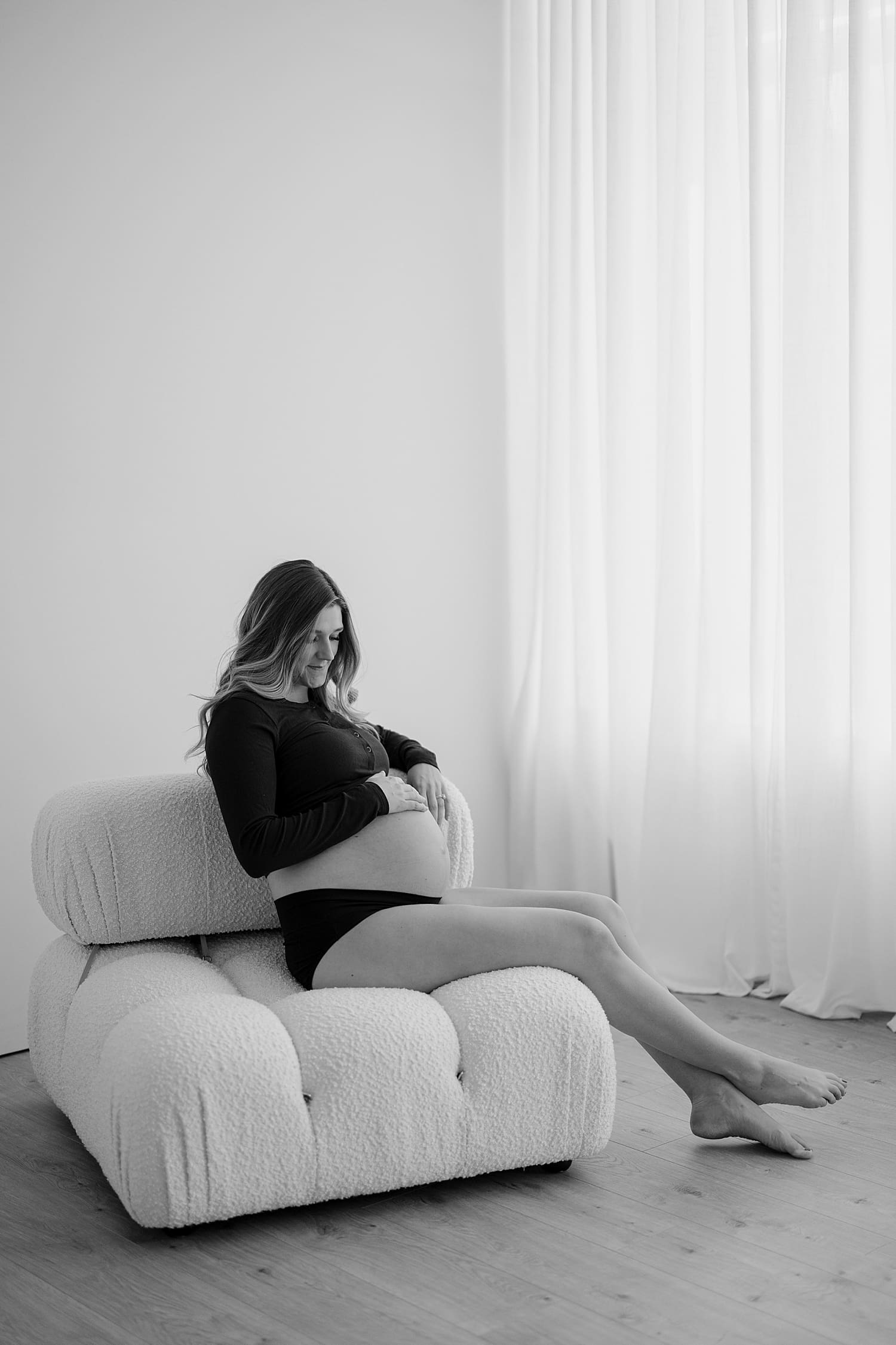 pregnant woman sits on big puffy chair by Rose and Oak Photography