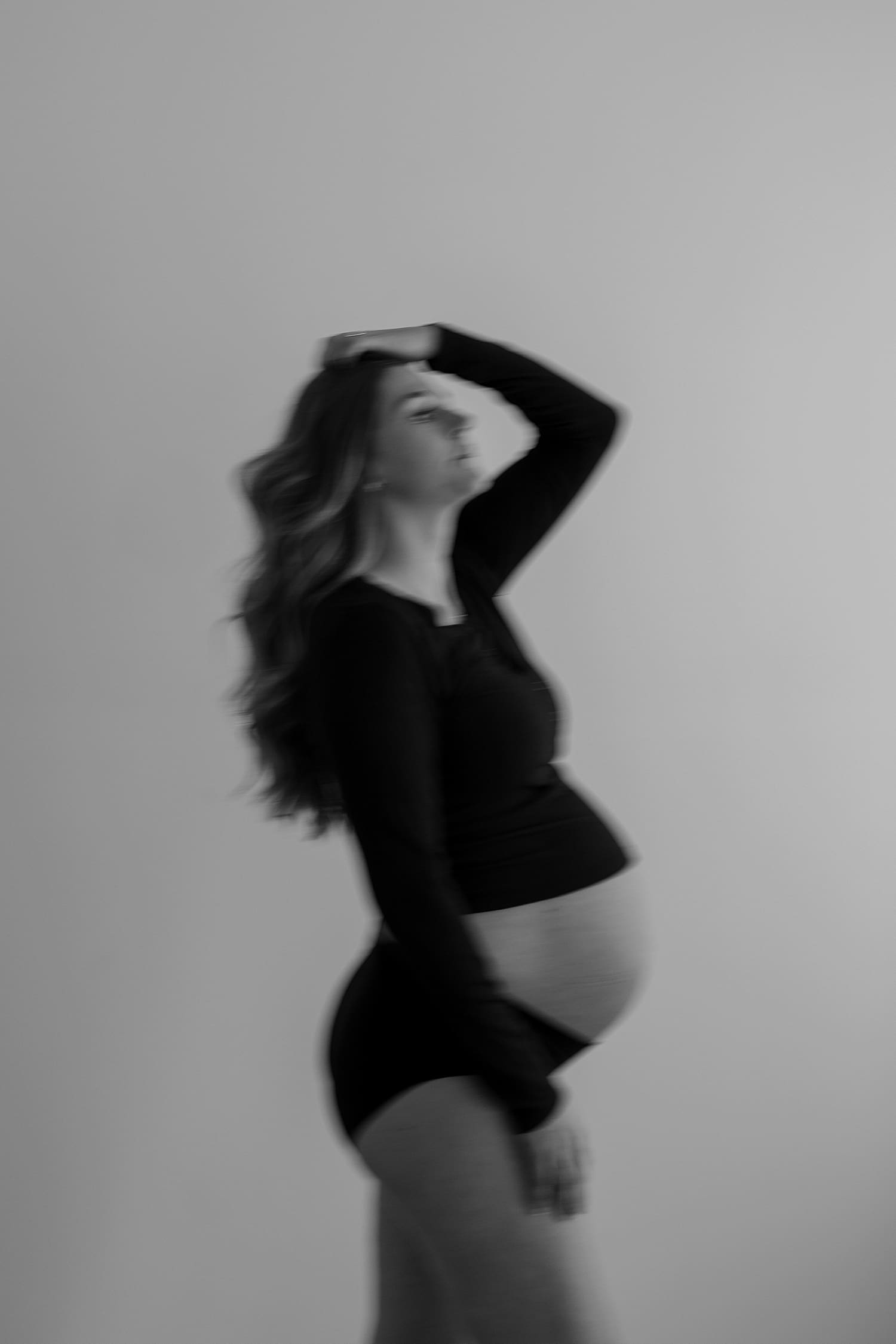 woman in long black tee and underwear stands against wall for classic studio maternity session