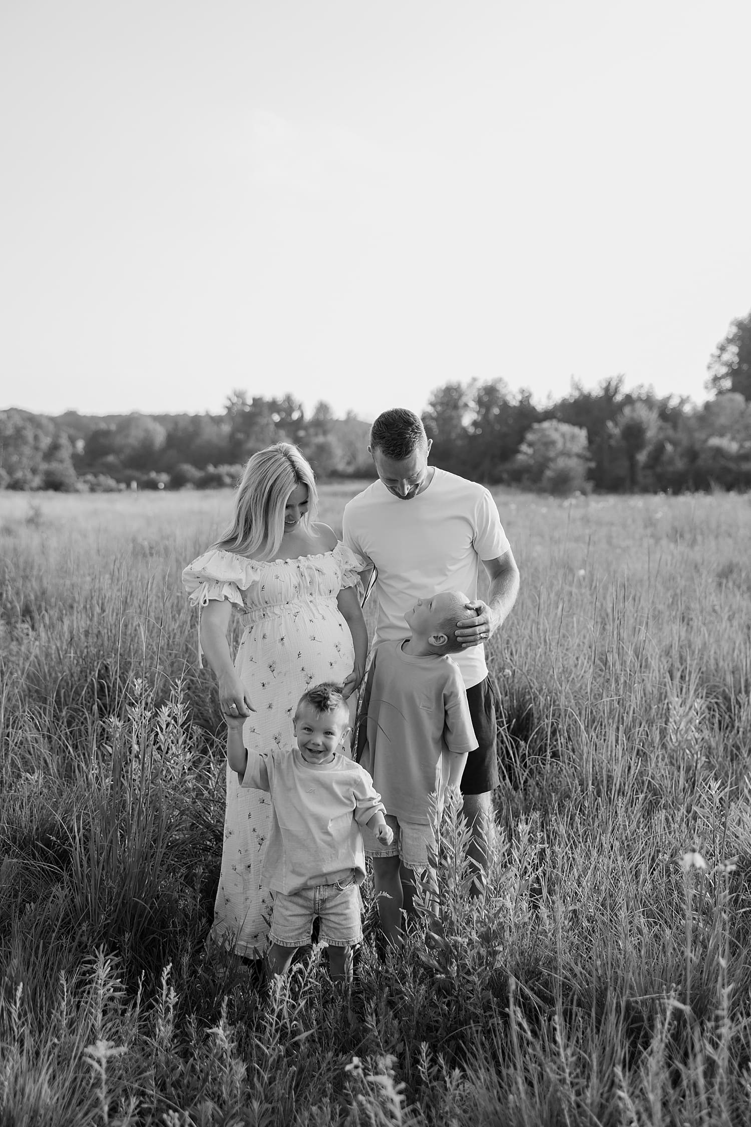 expecting mom looks at her two boys lovingly with husband nearby by Rose and Oak Photography
