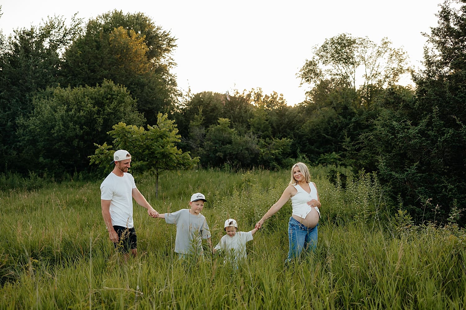 family of four walks through tall grass for golden hour maternity session