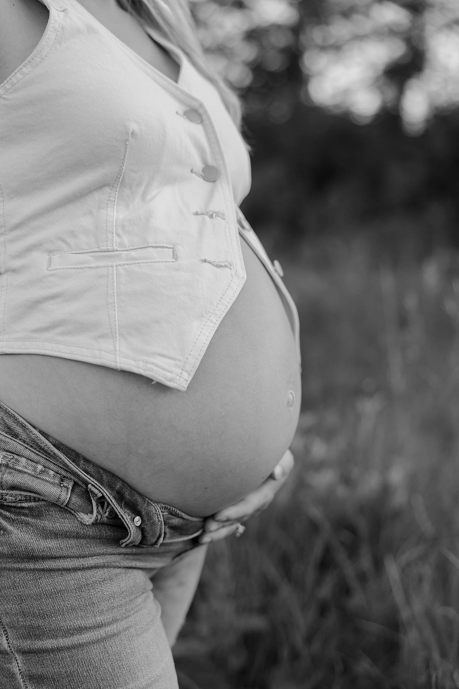 mother cradles expecting bump wearing jeans and vest by Wisconsin family photographer