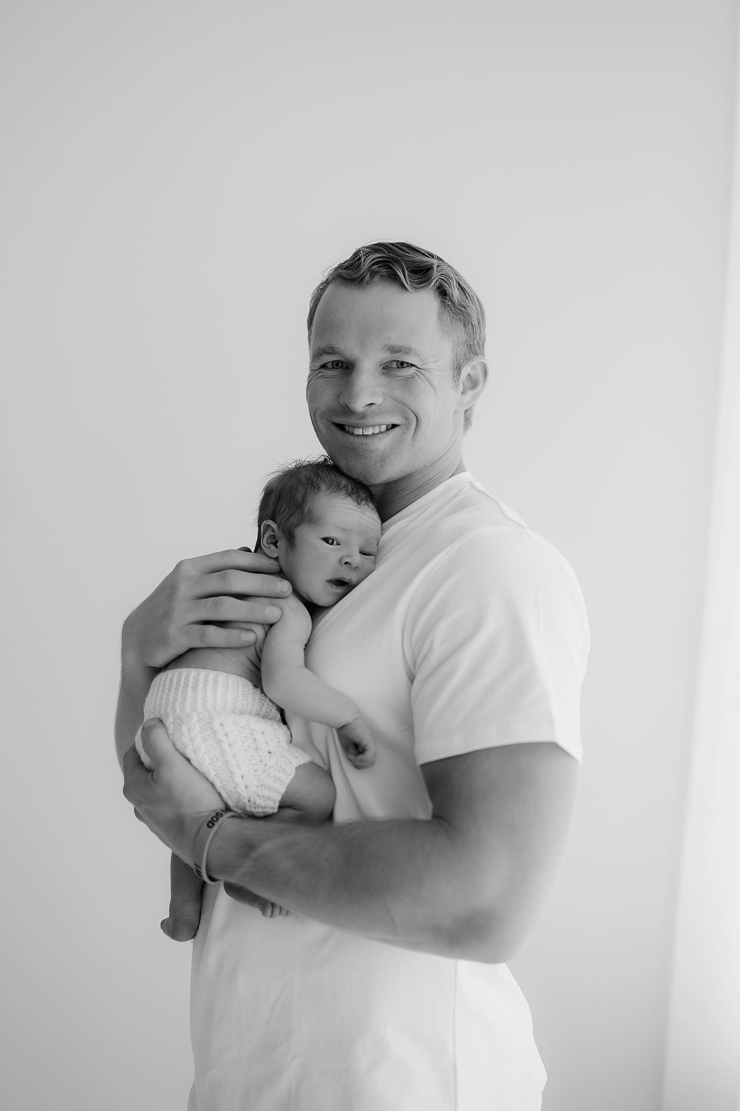 proud dad holds infant against his chest for neutral newborn session
