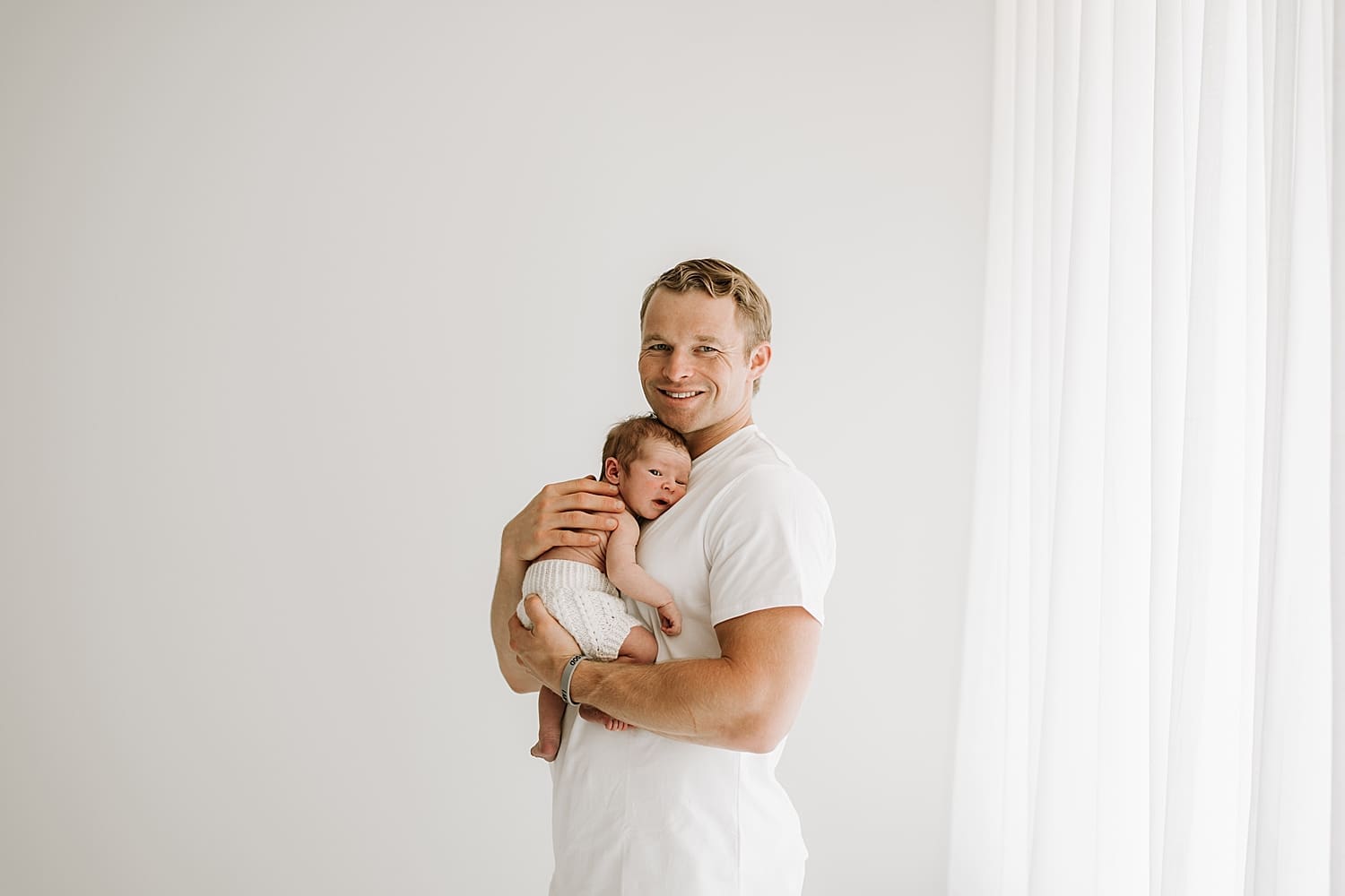 proud father snuggles new little one against chest by Wisconsin family photographer