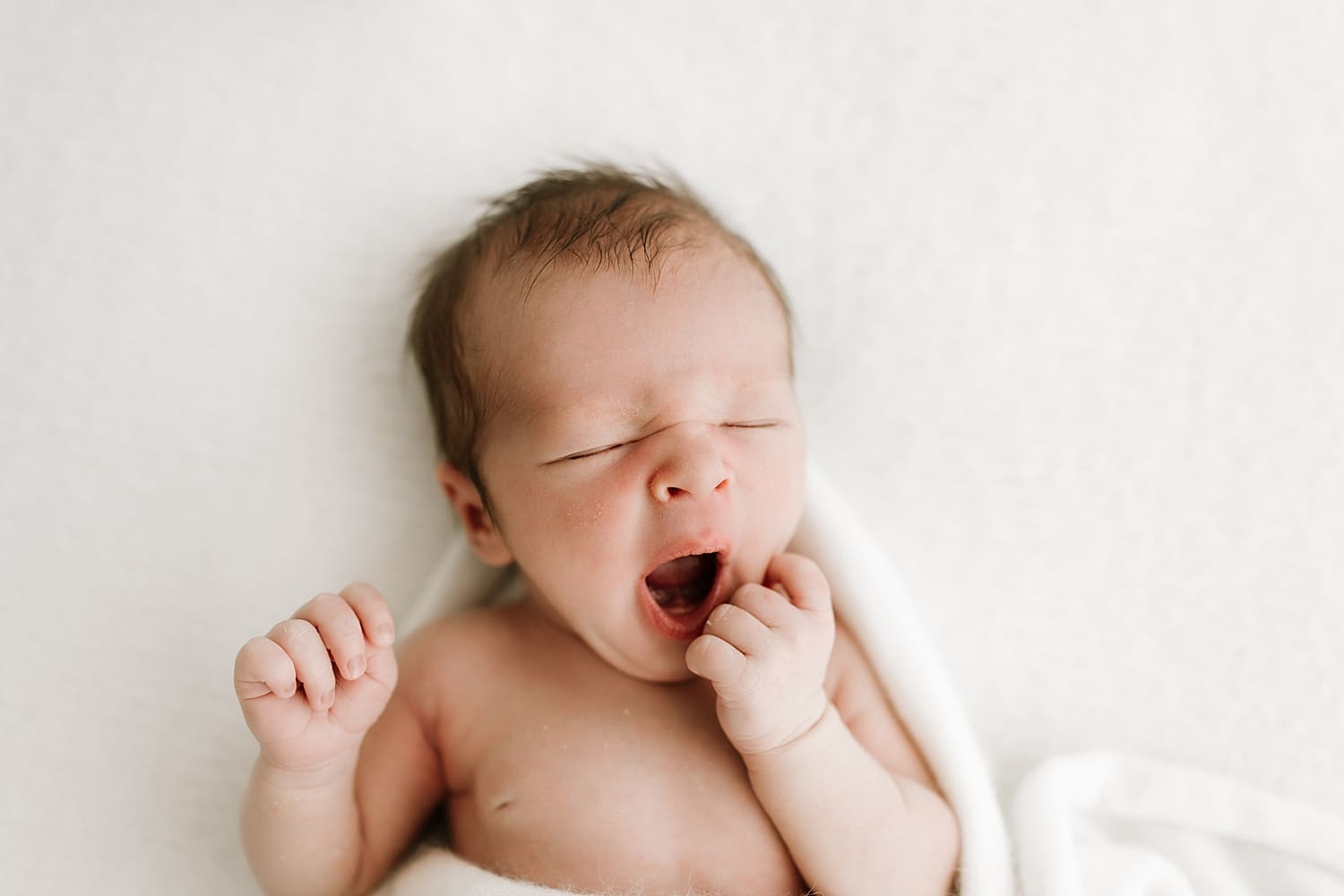 sweet infant yawns while surrounded with white fabric by Wisconsin family photographer