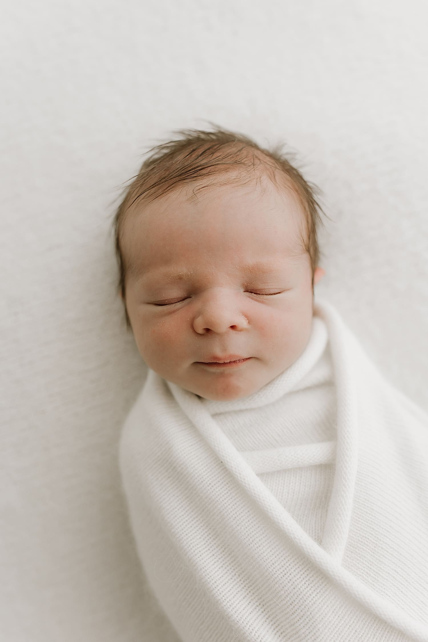 new infant wrapped in white on bed by Wisconsin family photographer