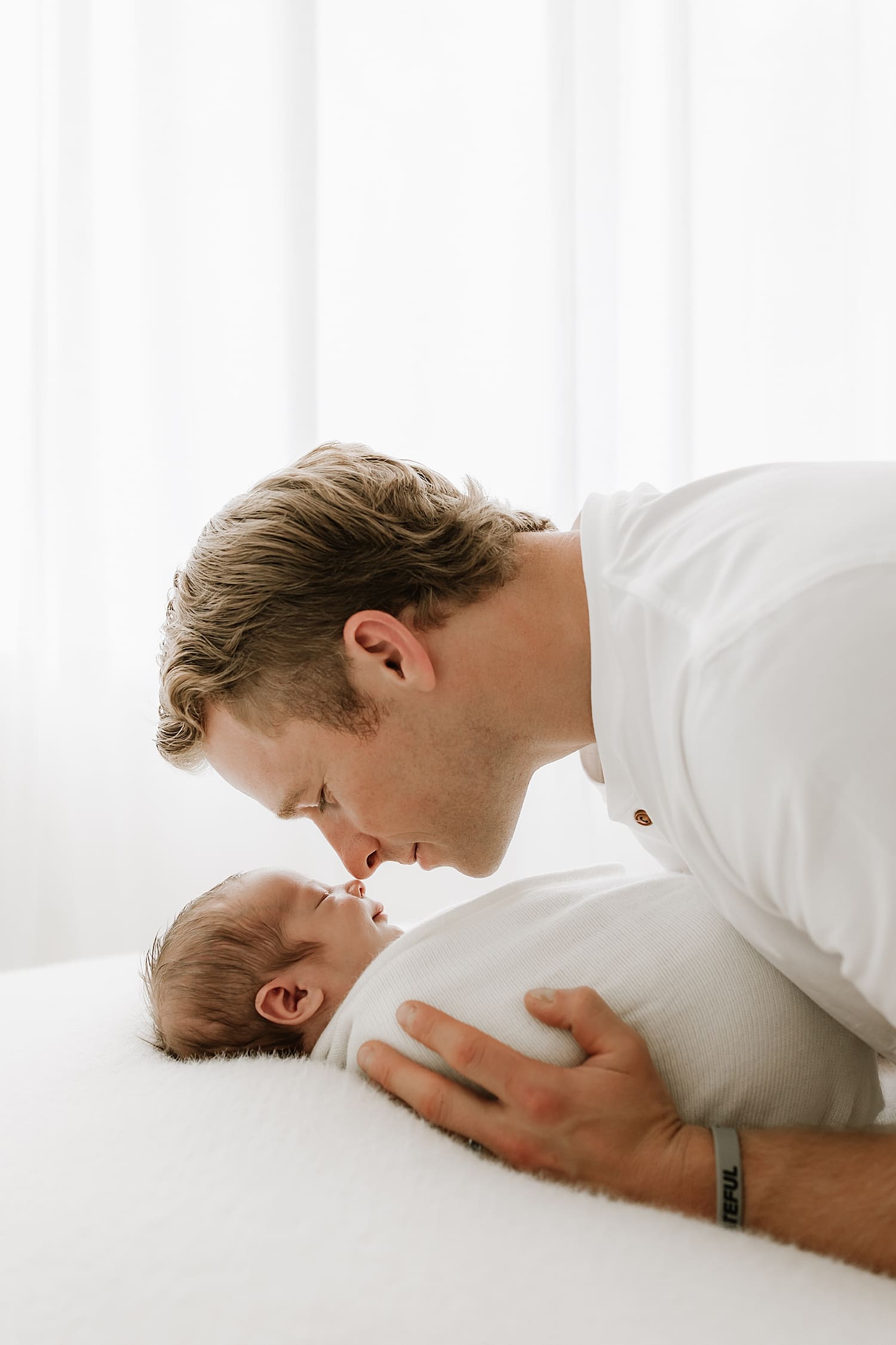 father leaning over infant wrapped on cushion for neutral newborn session