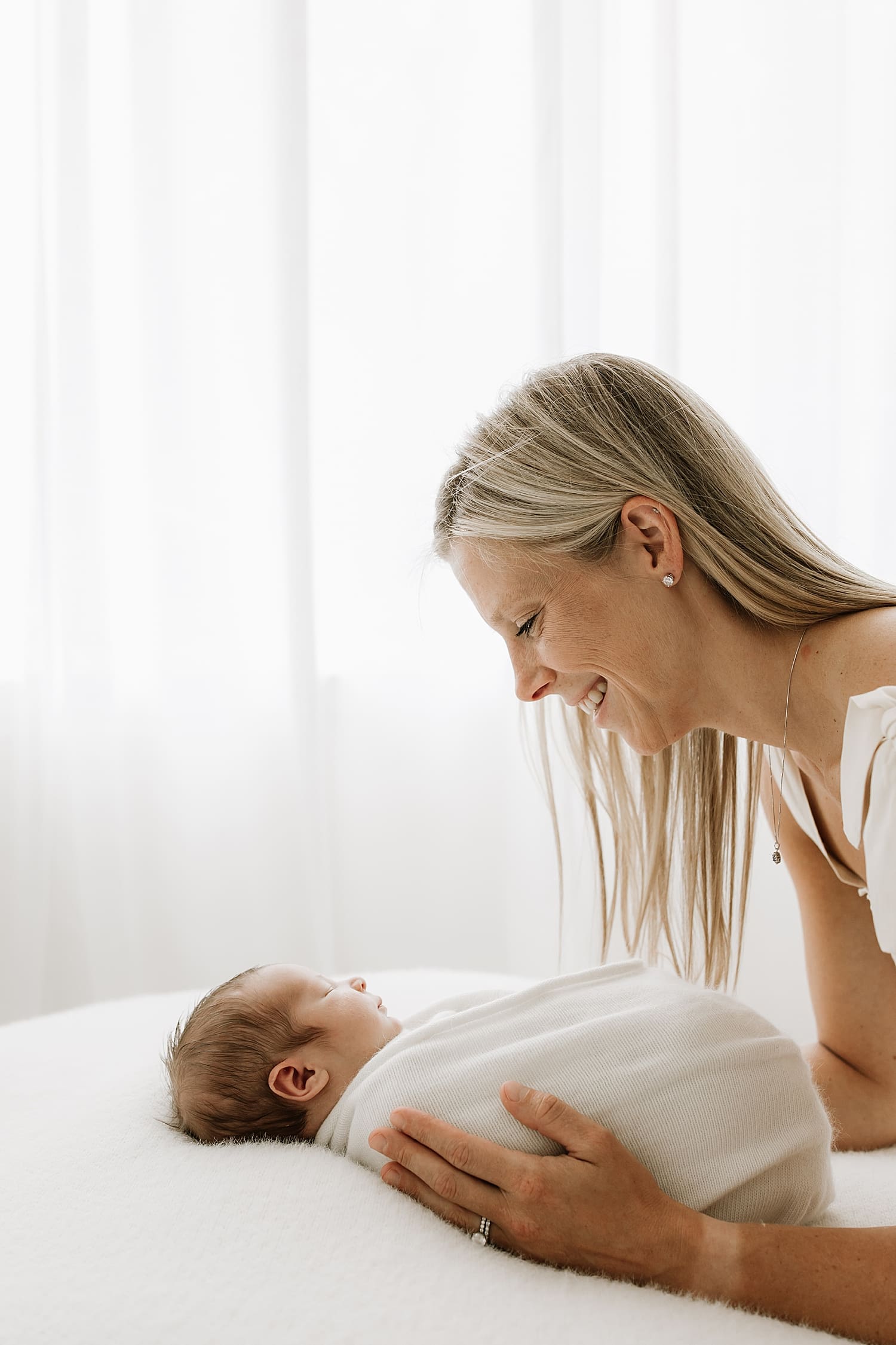 blonde in white dress leans over new little one wrapped on bed by Wisconsin family photographer