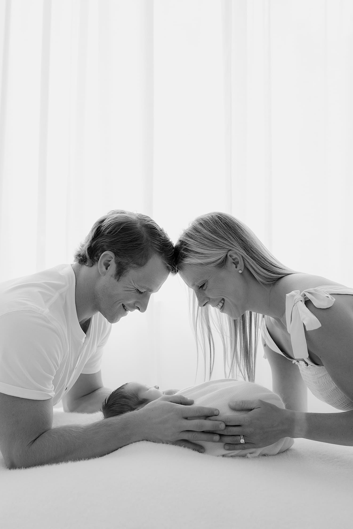 parents lean over their new bundle of joy together by Rose and Oak Photography