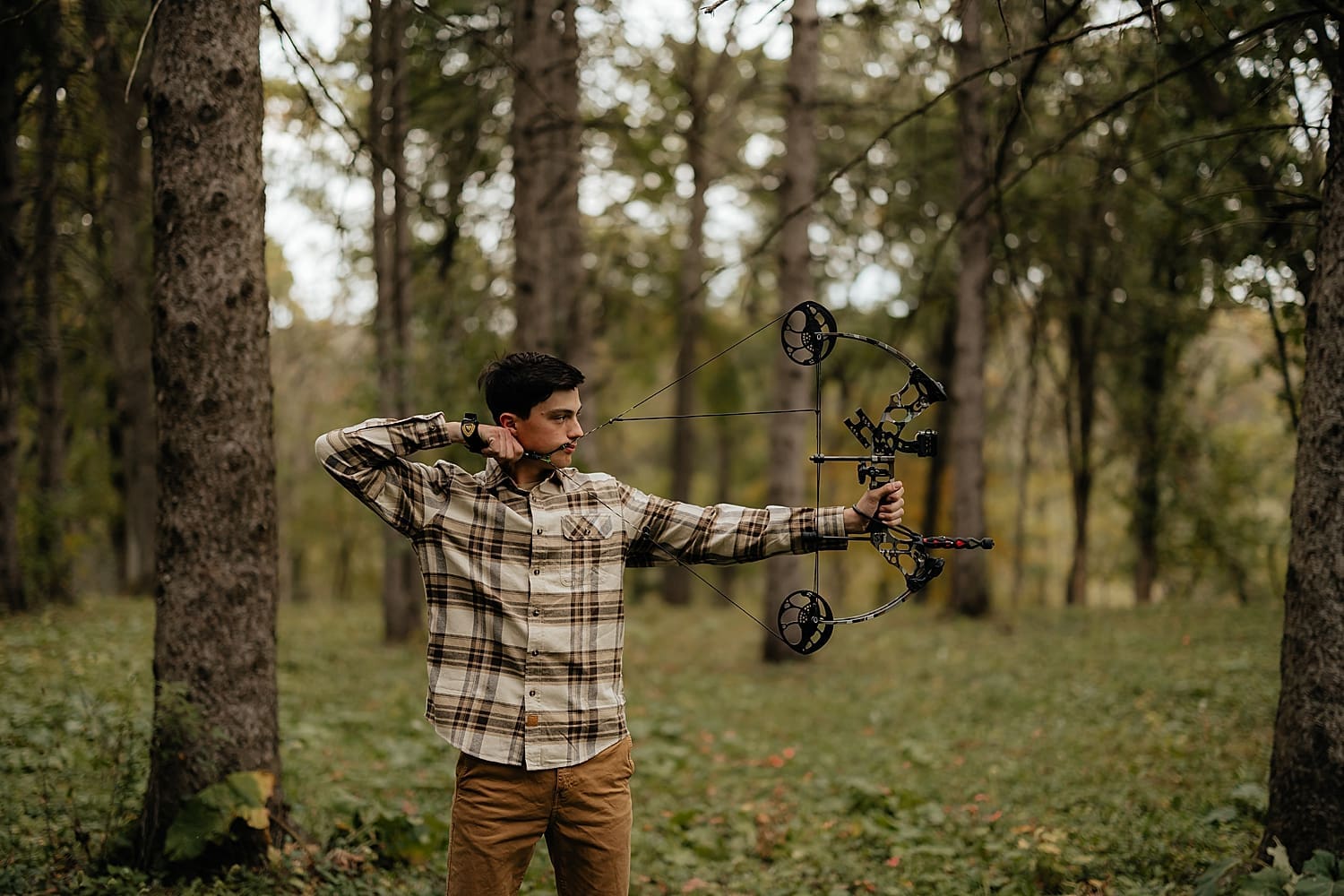 graduate stands in forest with bow by Rose and Oak Photography