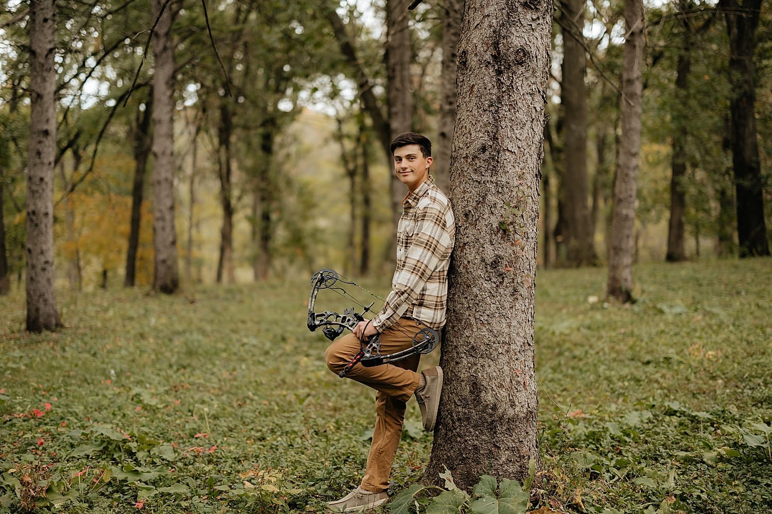 graduating student in plaid shirt leans against tree by Rose and Oak Photography