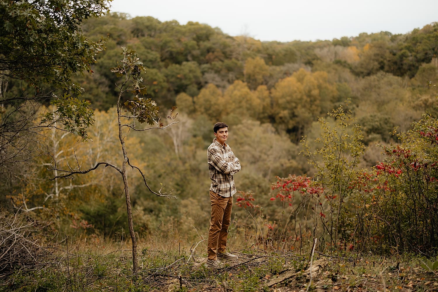 person stands with arms crossed in thicket for graduation photos by Wisconsin family photographer